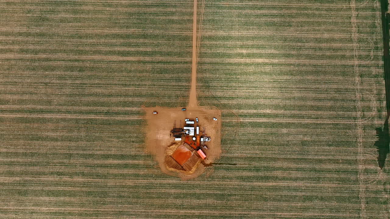 Going up over the site producing natural resources. Small location in the field with one tower rig in the center.