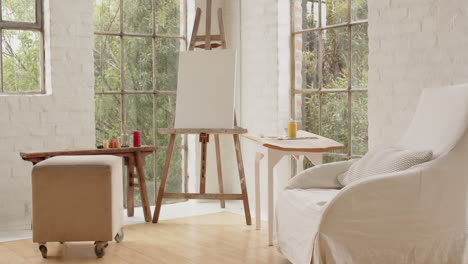 cozy art home studio with blank canvas and paints by large windows