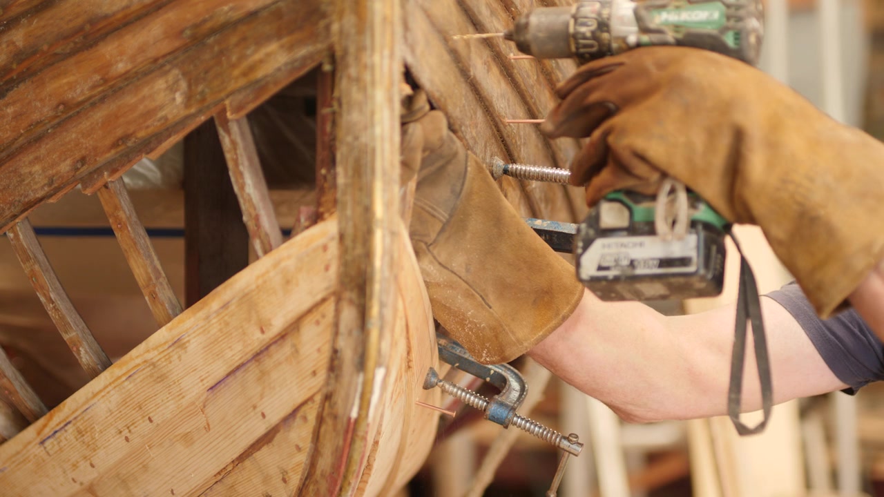 Pre-foratura di tavole dello scafo e costole di quercia per la riparazione di una barca in legno a clinker.