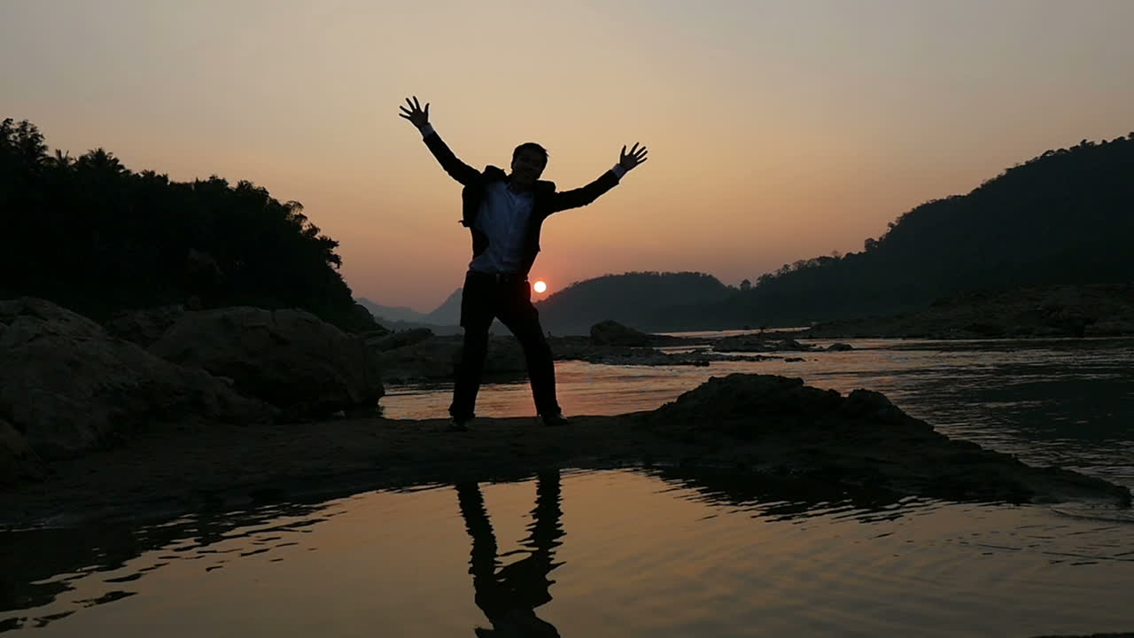 Silhouette of a man celebrating at sunset by a river