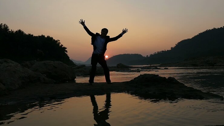 Silhouette di un uomo che festeggia al tramonto in riva a un fiume