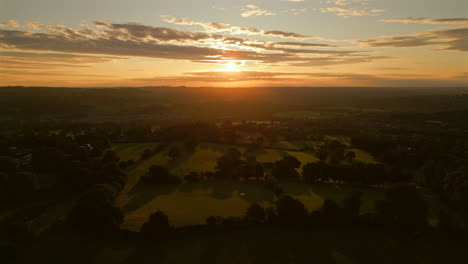 establishing drone shot into the sun over grass fields at golden hour sunrise