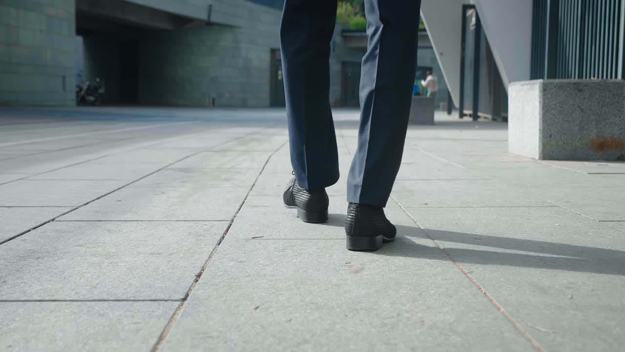 vista trasera pies de hombre de negocios que va a trabajar. vista trasera de hombre confiado empresario en zapatos de cuero y traje formal caminando por el centro cerca de un edificio de oficinas.