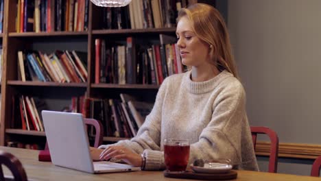 mujer sonriente usando una laptop en la biblioteca