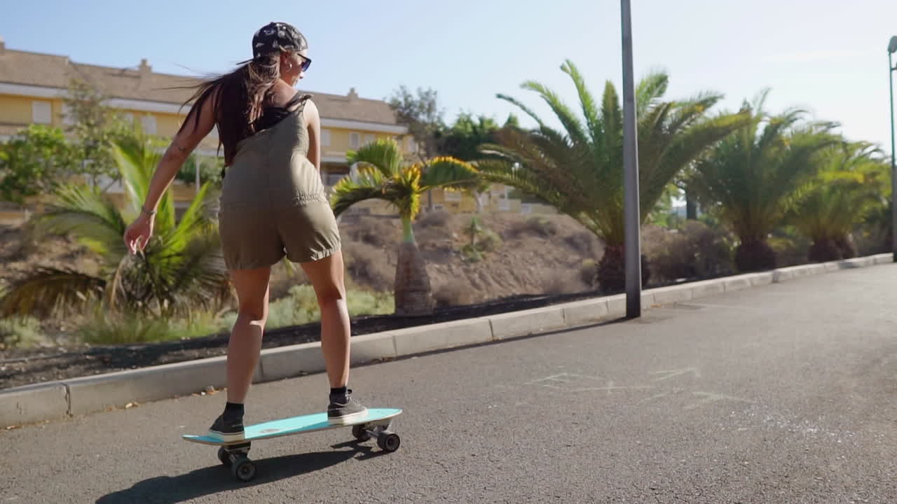 en la gracia de la cámara lenta, una hermosa chica se desliza en su longboard a lo largo de la carretera cerca de la playa y las palmeras