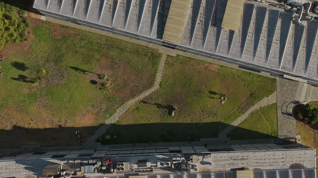 Top-down spiral descending drone movement grassy urban park beside modern buildings, Málaga, Spain