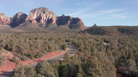 aerial: shot in sedona arizona of a car driving through rock formations and a beautiful landscape on a sunny day