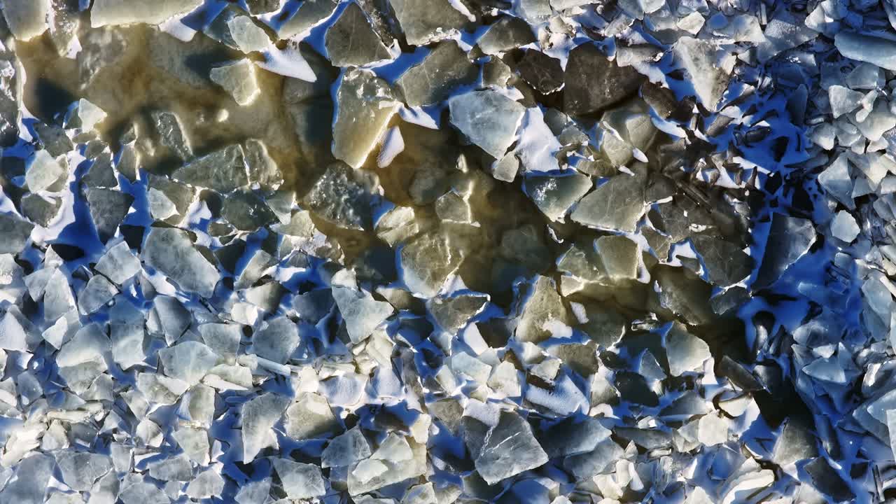 Fractured ice covering frozen sea surface, creating patterns of cold and winter environment in aerial top down view