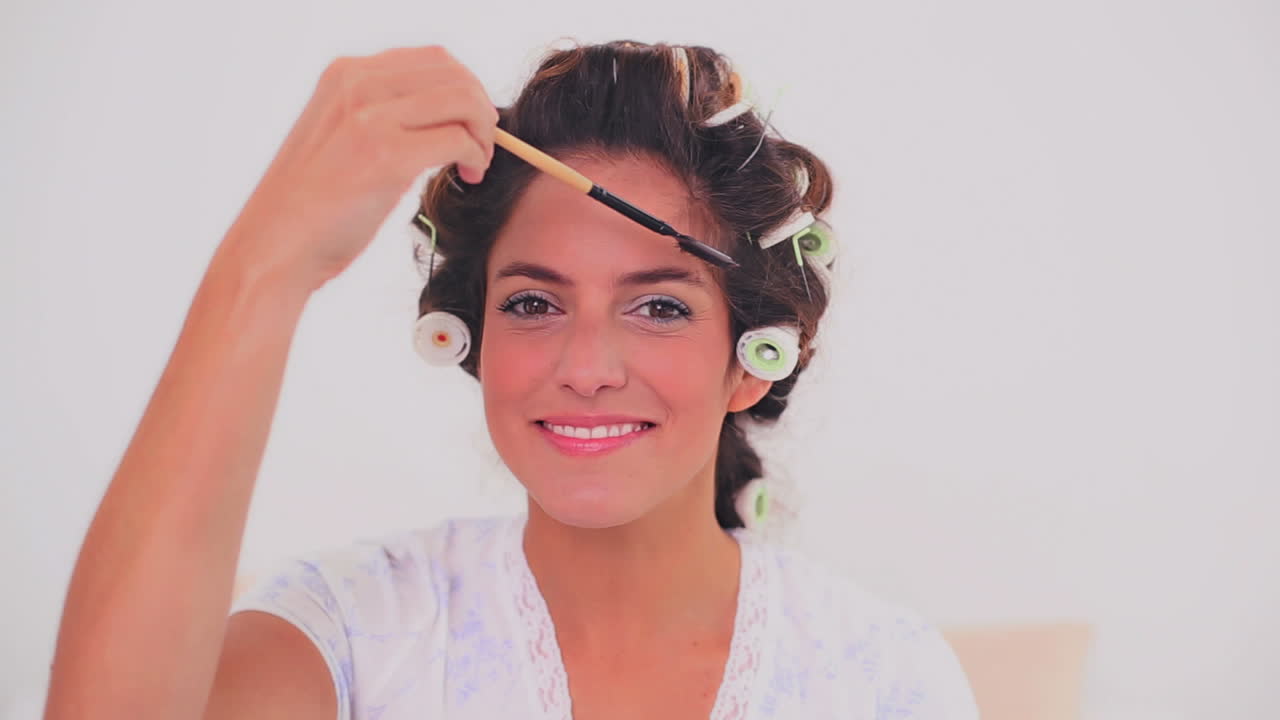 Smiling woman in hair curlers brushing her eyebrows