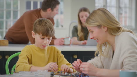 Mother-helping-son-with-electronics-project-sitting-at-kitchen-table-at-home-with-laptop---shot-in-slow-motion