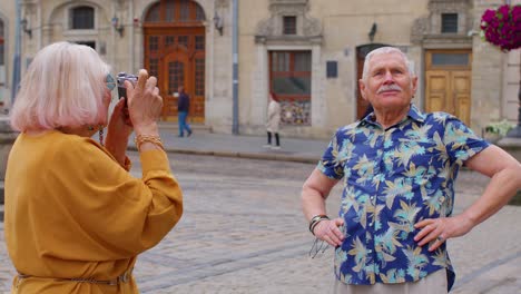 elderly tourist grandfather taking photo pictures of grandmother on retro camera in old summer town