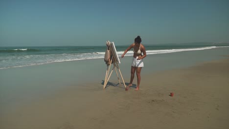 long shot of a young artist painting on a sunny beach, an elegant female paints artistic expression outdoors