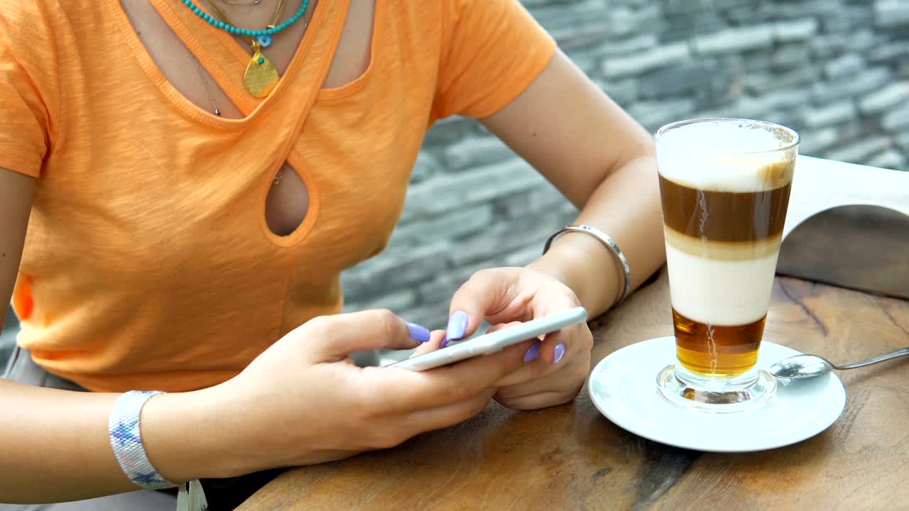 4k joven atractiva usando su teléfono y bebiendo de una taza de café en una cafetería