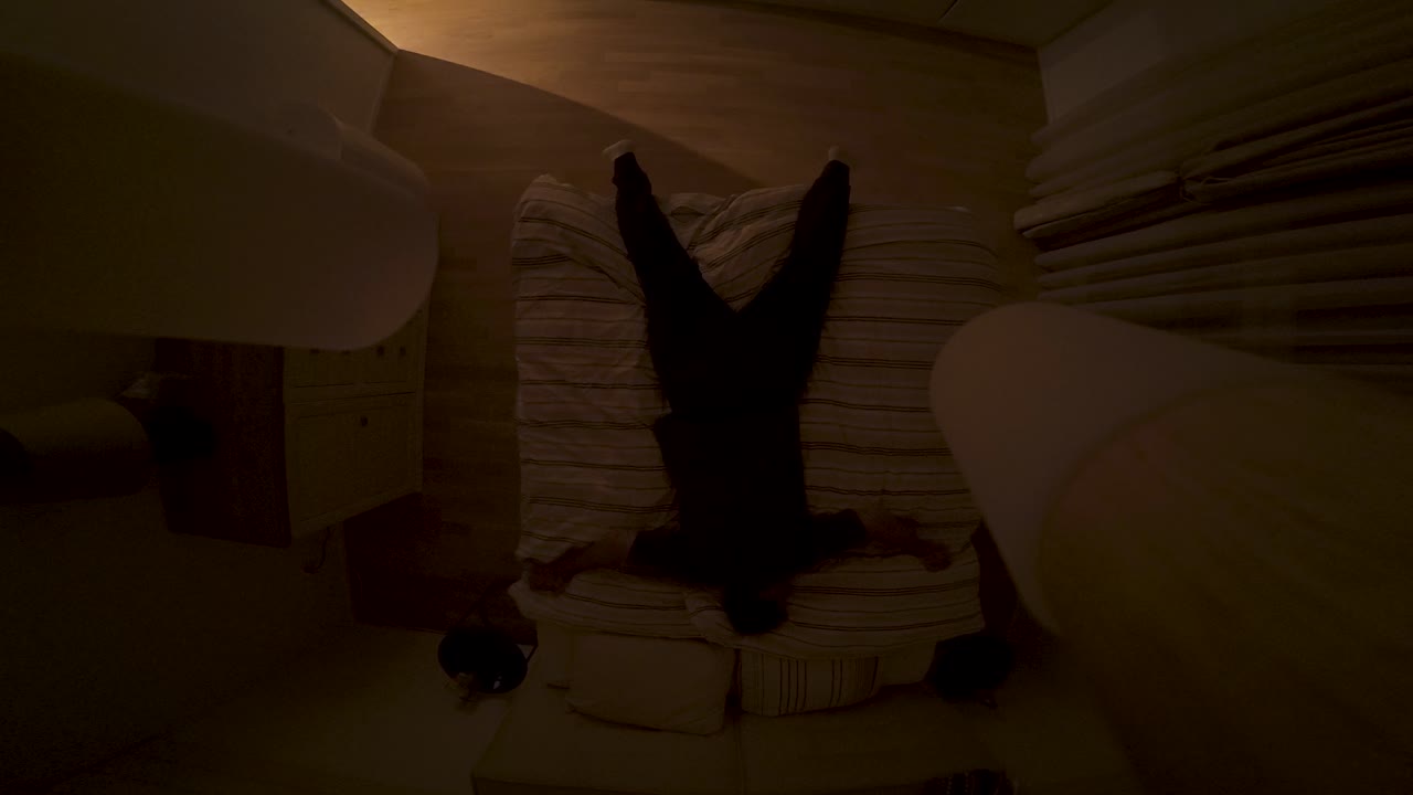 A man exhausted from the day falls onto his bed in the evening, captured from an overhead view