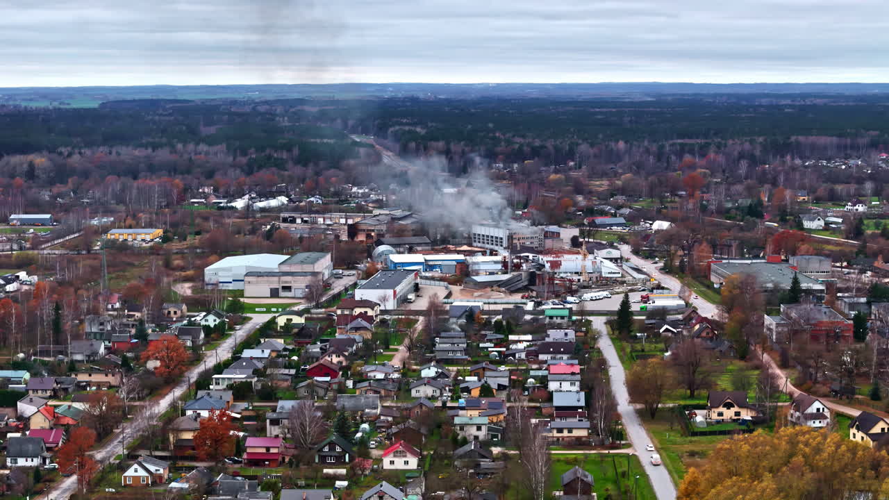 집과 나무로 둘러싸인 산업 구역에서 연기가 아오르는 작은 마을, 공중 사진