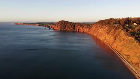 aerial of sidmouth coastline peak hill  bathed in golden sunrise light in the morning. dolly right