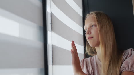 Teenage-girl-sitting-on-the-windowsill,-looking-out-the-window