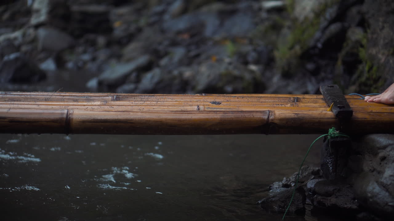 Woman walking across a bamboo bridge over a river