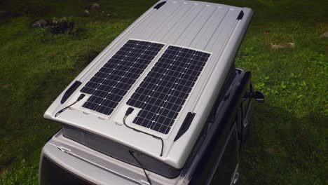 orbit drone shot of silver camper van with two solar panels on opened pop top roof tent