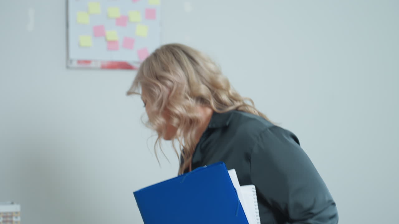 Close up of elegant professional woman turning to take seat in office, holding file and preparing to drop it on desk, with softly lit background and modern decor suggesting calm work environment