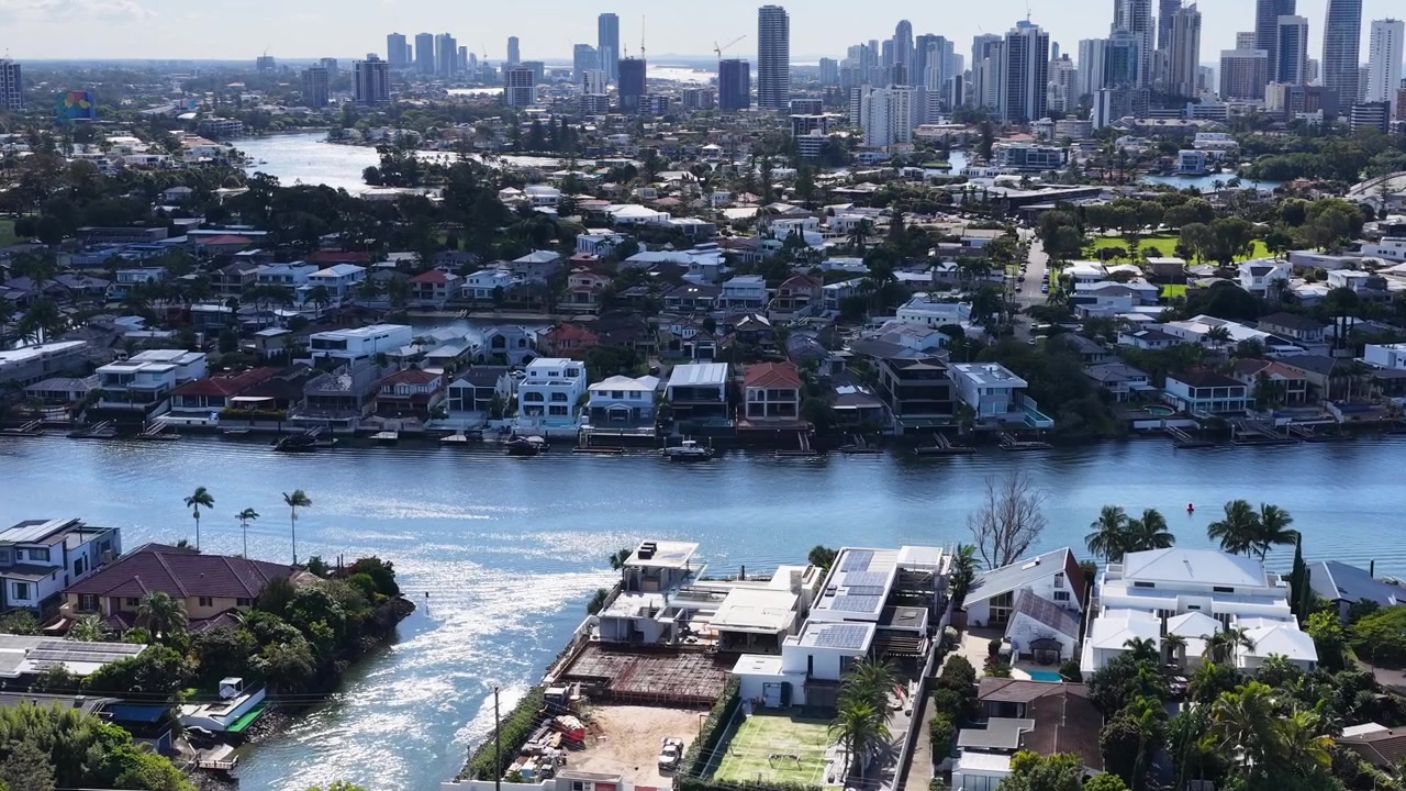 Ampia ripresa aerea con drone che si muove su lussuose abitazioni fronte mare e lontani grattacieli urbani illuminati dal sole.