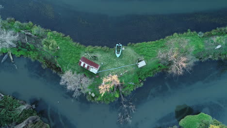 white swan moving slowly along river, beside a cabin and boat on small land mass