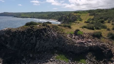 flying over rock coastline of maui, hawaii on sunny day, dolly forward up and over then lower to water
