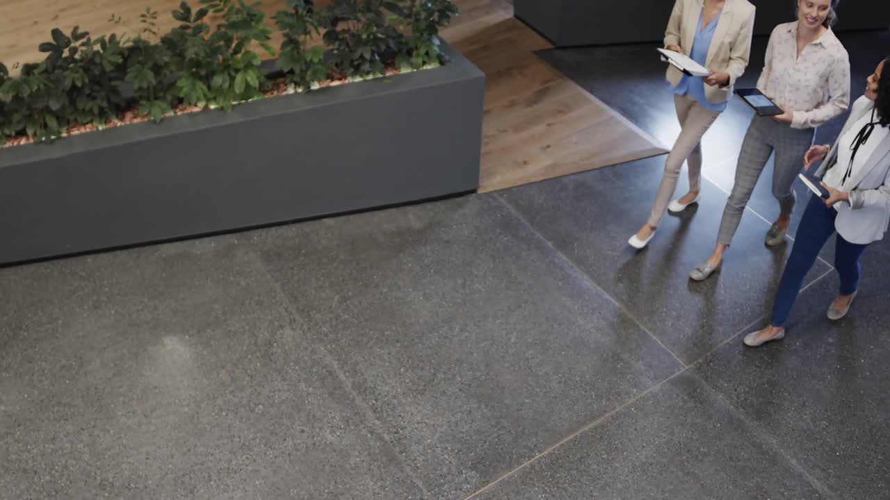 diversas compañeras en discusión usando tableta en el vestíbulo de la oficina, cámara lenta