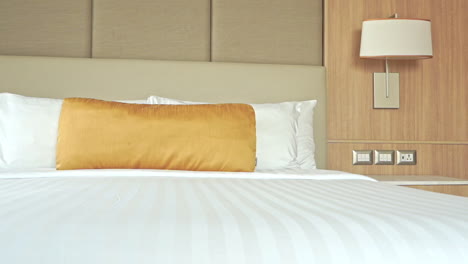 close-up pan across a large comfortable hotel bed decorated with a gold throw pillow