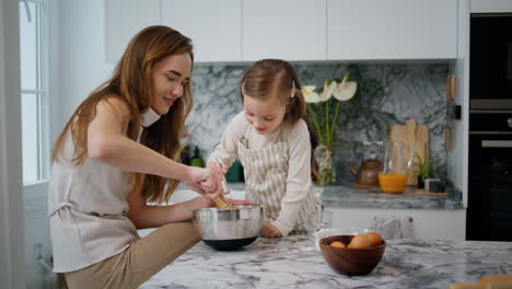 cheerful family making dough at home. girl helping millennial mom at kitchen