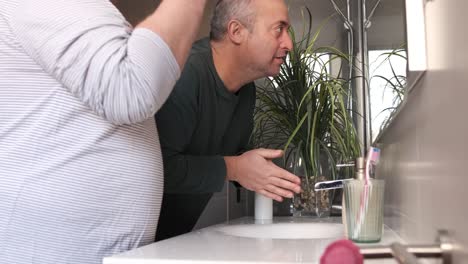 mature homosexual couple cleaning face and teeth in the toilet at home