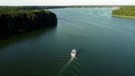 small yacht driving on a lake surrounded by a forest in brandenburg, germany