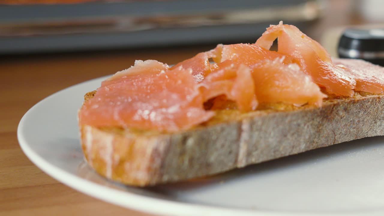 Fresh Seafood Smoked Salmon Fish Fillets Being Placed on Baked Sourdough Bread by Female Hand in Kitchen Setting with Natural Sunlight 4K. Healthy Breakfast.