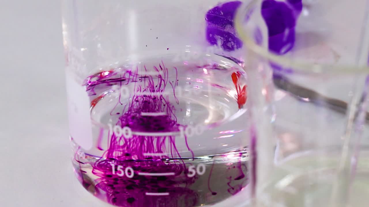 En detaljerad närbild som visar hur lila färg diffunderar och blandas i en laboratoriebägare av klart glas