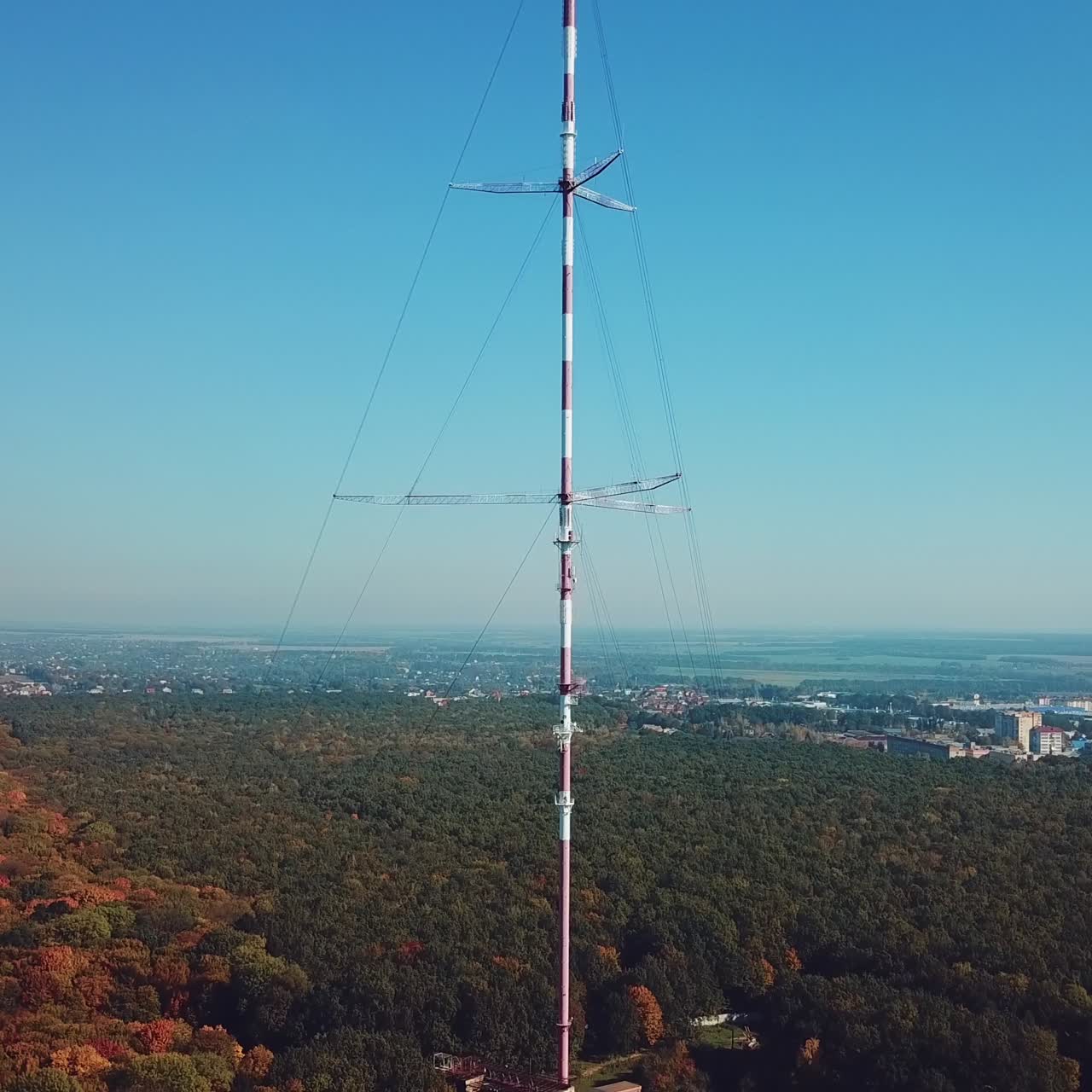 high telecommunication antenna on the background of forest and cityscape. Camera motion up