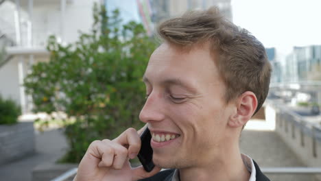 Un-Joven-Caucásico-Hablando-Por-Teléfono-Afuera,-Luciendo-Emocionado