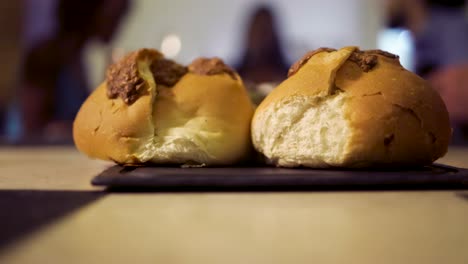 close up view of bread in the foreground while people are eating and having great conversation at an outdoor dinning restaurant in the background