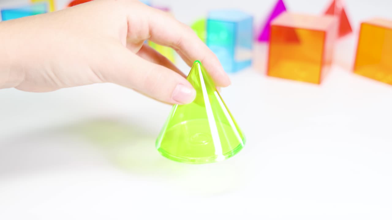 Hands manipulate vibrant 3D geometric shapes on a white surface, emphasizing educational play and tactile learning