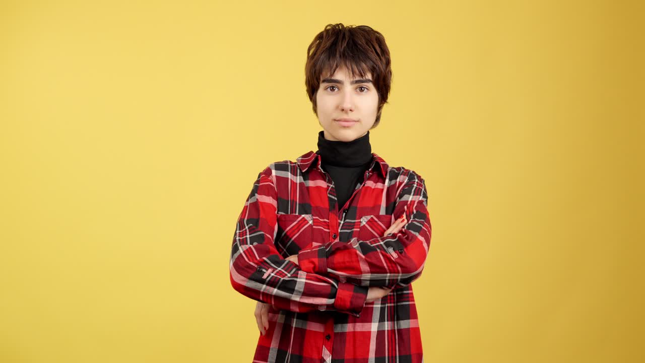 Young person with short hair and plaid shirt standing confidently against a yellow background