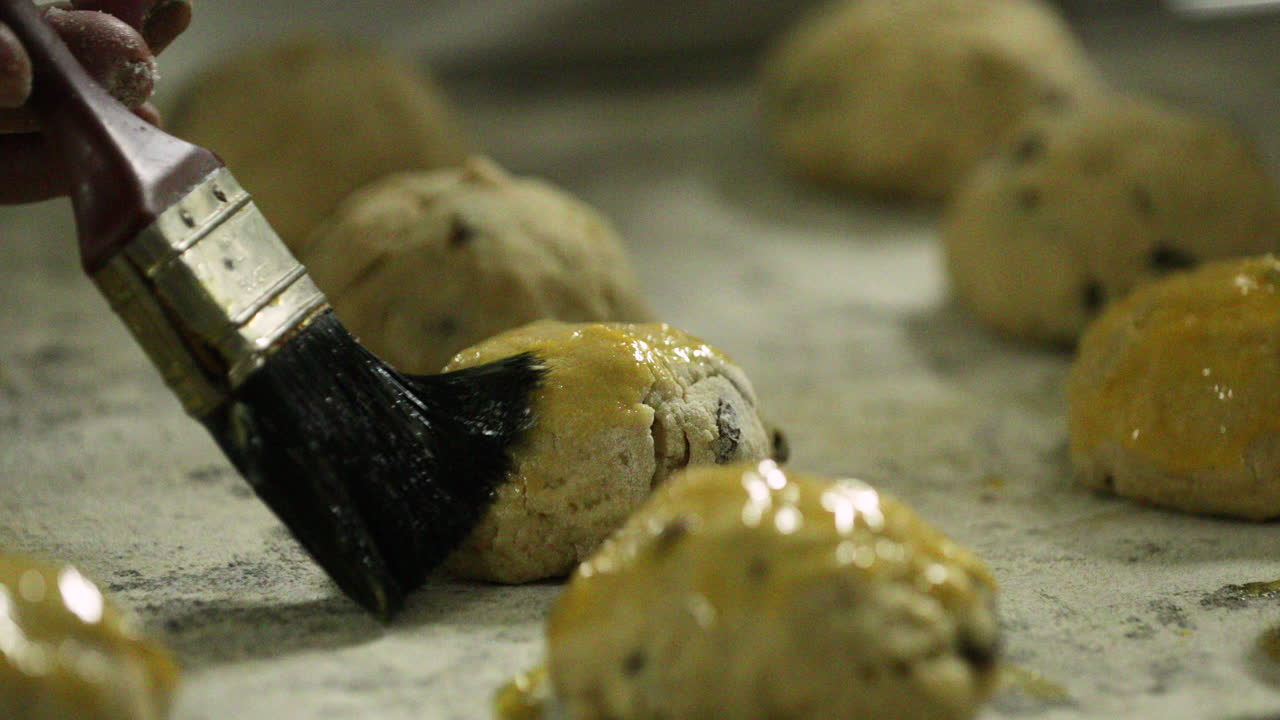 Baker Applying Egg Wash With A Pastry Brush To Raisin Cookies On A Tray Before Baking - slow motion
