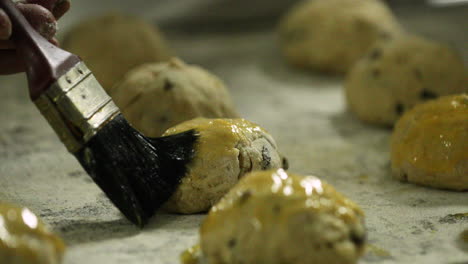 baker applying egg wash with a pastry brush to raisin cookies on a tray before baking - slow motion