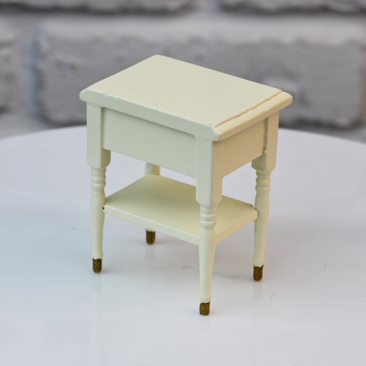 Toy wooden piece of furniture in studio. Tiny white nightstand with a cute drawer and shiny golden knob. Toy furniture circling isolated against wall background