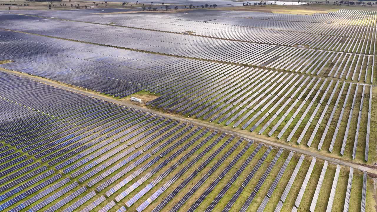 Drone camera pans across expansive photovoltaic solar panels under partly cloudy sky, natural daylight