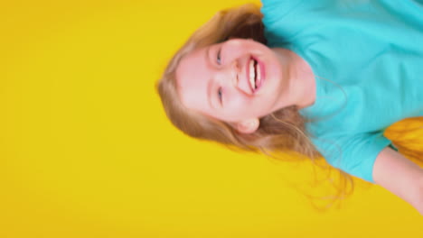 Vertical-Video-Of-Girl-With-Long-Hair-Laughing-And-Spinning-Against-Yellow-Background