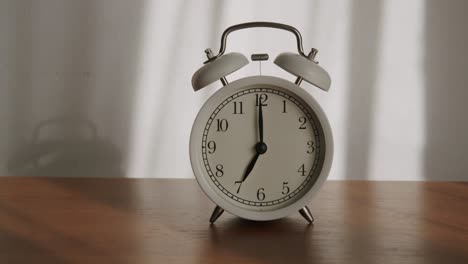 white alarm clock is placed on a wooden table and the light shines through the curtains in the morning.