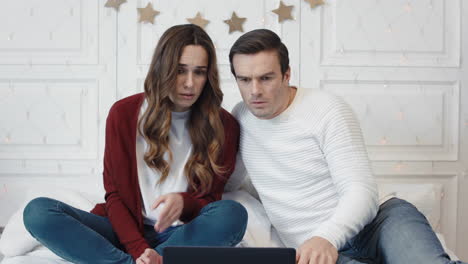 una pareja estresada viendo noticias horribles en la computadora en casa juntos.