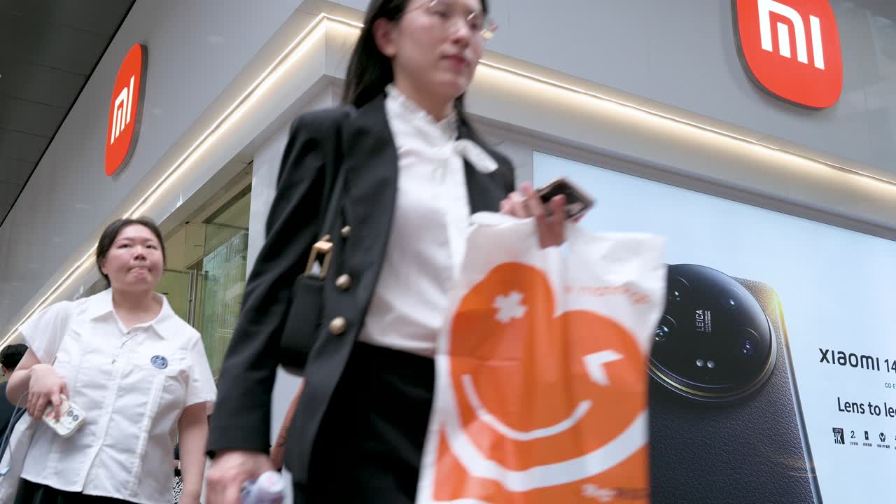 A low-angle view of a crowded flow of pedestrians walking past the flagship store of the Chinese multinational technology and electronics brand, Xiaomi, in Hong Kong, China.