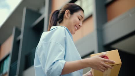 close up parcel in hand of blue uniform delivery man to customer front of the house with good service from shopping online. courier man delivering a cardboard box postal package to destination.