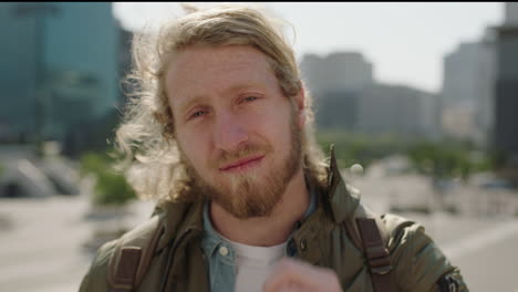 portrait-of-young-blonde-man-student-with-beard-looking-at-camer-confident-running-hand-through-hair-in-urban-city-background