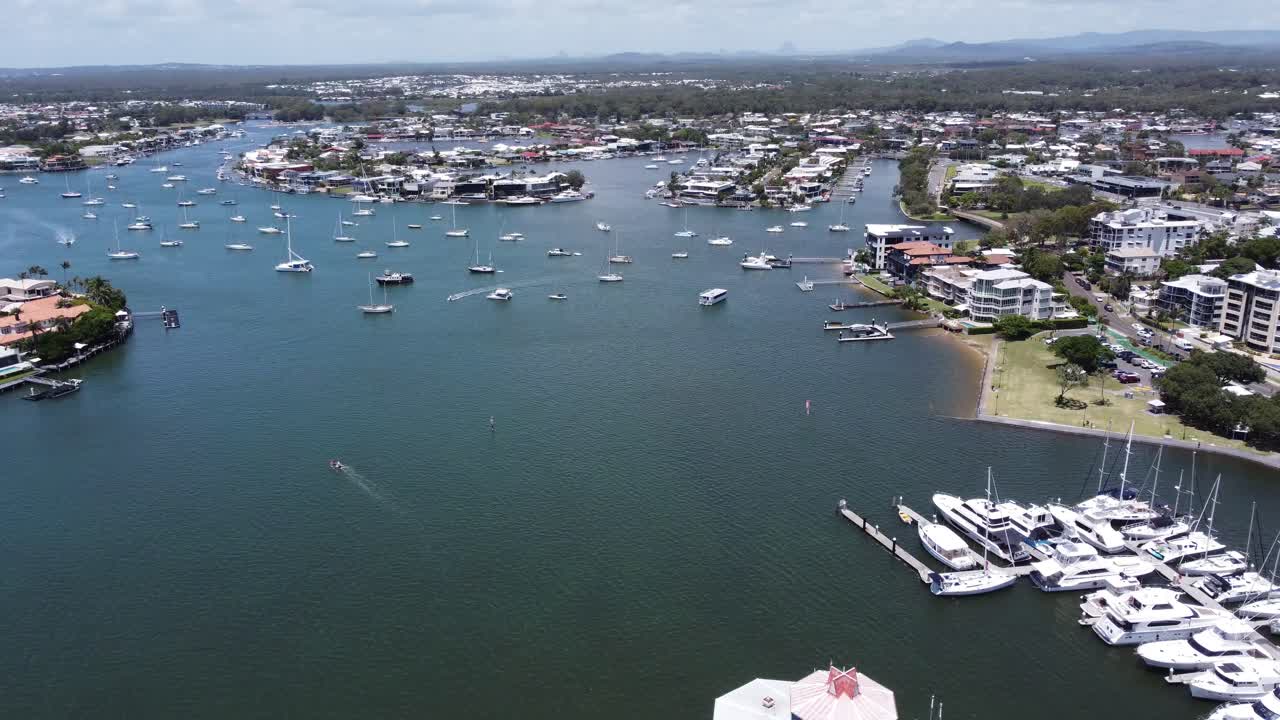 Drone ascending over a large boat harbour with high-rise holiday apartments in the background